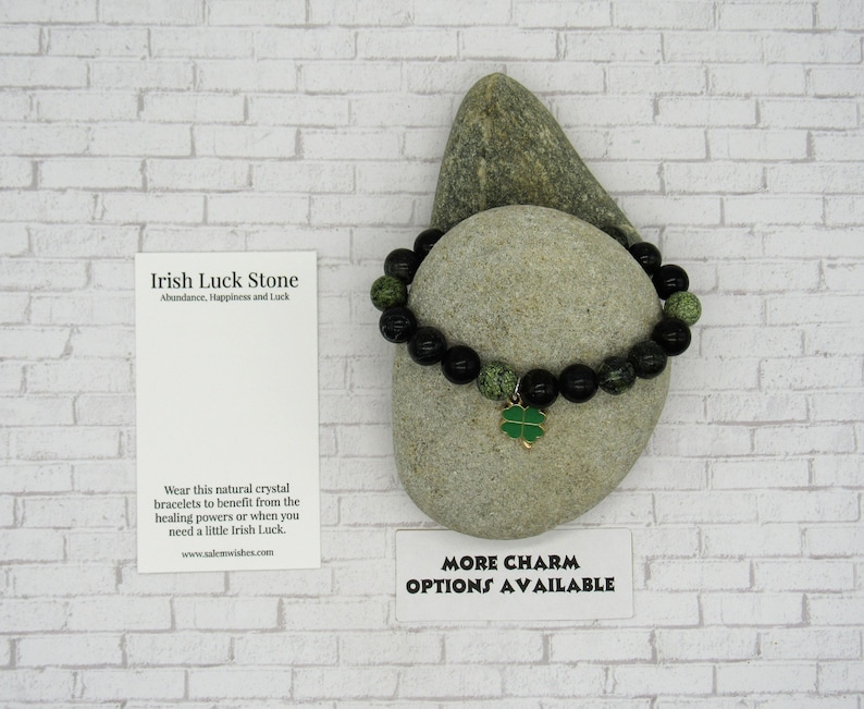 K&ouml;nnte beinhalten: Schwarzes und gr&uuml;nes Perlenarmband mit einem goldenen Kleeblatt-Anh&auml;nger. Das Armband liegt auf einem grauen Stein mit einer wei&szlig;en Karte, auf der "Irish Luck Stone Abundance, Happiness and Luck" und "Wear this natural crystal bracelets to benefit from the healing powers or when you need a little Irish Luck. www.salemwishes.com" steht. Die Karte tr&auml;gt au&szlig;erdem den Text "More Charm Options Available".