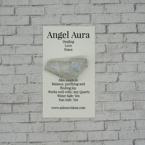 May include: A white Angel Aura crystal with iridescent shimmer. The card reads "Angel Aura", "Healing", "Love", "Peace", "Also Aues in: Balance, purifying and finding joy.", "Works well with: Any Quartz", "Water Safe: Yes", "Sun Safe: Yes", "www.salemwishes.com".