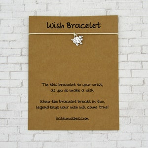 May include: A brown card with white string and a silver charm of a sheep. The card reads "Wish Bracelet" and includes instructions to tie the bracelet to your wrist and make a wish. The card also says that when the bracelet breaks in two, legend says your wish will come true. The card is signed "Salemwishes.com".