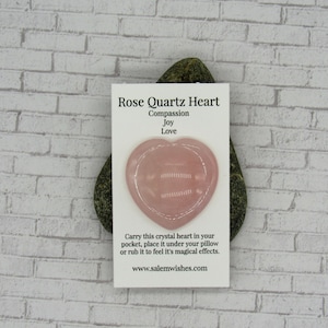 May include: A pink rose quartz heart shaped crystal on a white card with the text "Rose Quartz Heart, Compassion, Joy, Love, Carry this crystal heart in your pocket, place it under your pillow or rub it to feel it's magical effects. www.salemwishes.com"