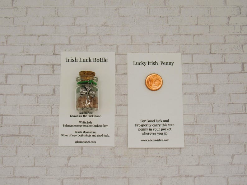 May include: A white card with the text "Irish Luck Bottle" and a small glass bottle with a green shamrock charm and pink and white stones inside. The card also includes information about the stones, including "Avemunine", "White Jade", and "Peach Moonstone".