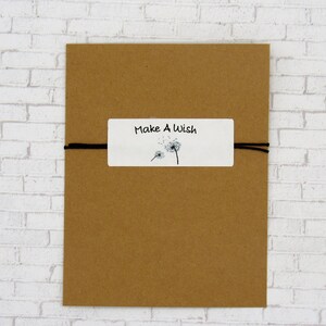 May include: A brown paper envelope with a white label that says "Make A Wish" and has a black and white illustration of dandelions. The envelope is tied with a black string.