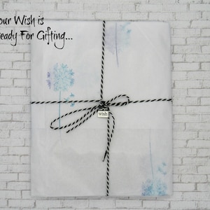 May include: A wrapped gift, covered in white paper with blue dandelion designs. The package is tied with black and white twine and a small silver charm that says "wish". The text "Your Wish is Ready For Gifting..." is printed on the top left.