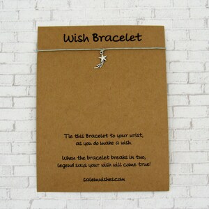 May include: A brown card with the text "Wish Bracelet" printed on it. The card has a gray string with a silver shooting star charm attached to it. The text on the card reads: "Tie this Bracelet to your wrist, as you do make a wish. When the bracelet breaks in two, legend says your wish will come true! salemwishes.com"