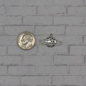 May include: Silver charm of a planet with a ring and stars. The charm is about the size of a US dime.
