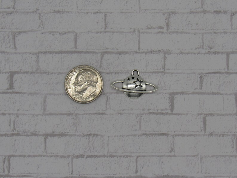 May include: Silver charm of a planet with a ring and stars. The charm is about the size of a US dime.
