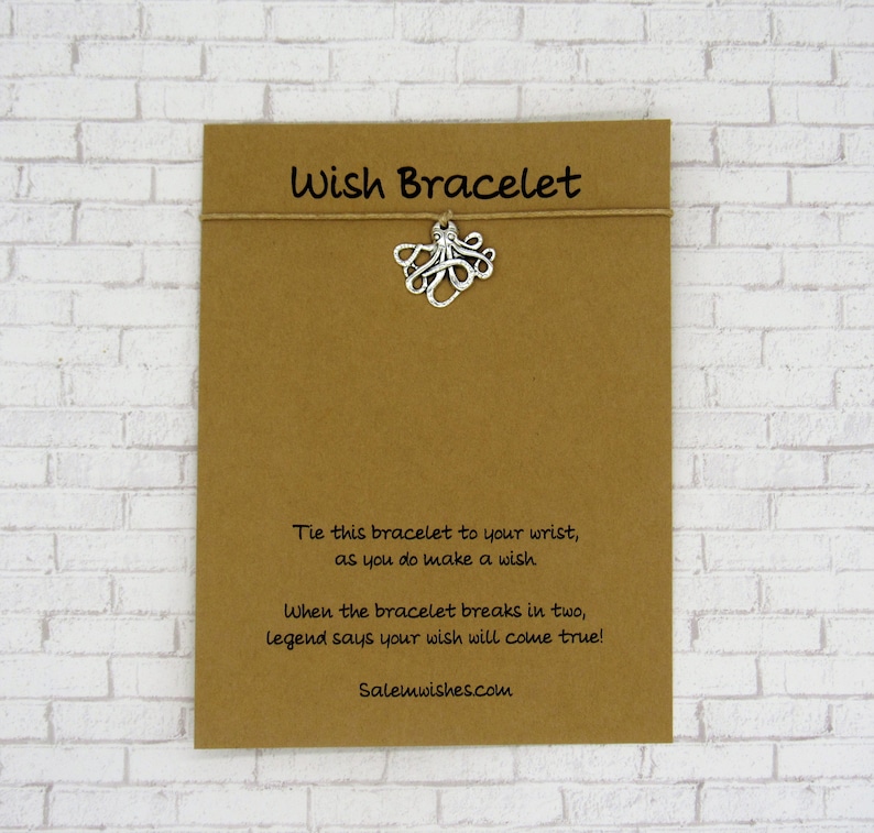 May include: A brown card with the text "Wish Bracelet" printed in black. The card has a silver octopus charm attached to a string. The text on the card reads: "Tie this bracelet to your wrist, as you do make a wish. When the bracelet breaks in two, legend says your wish will come true! Salemwishes.com"
