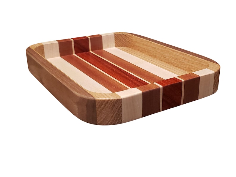 Op de afbeelding: Een rechthoekige houten dienblad met een gestreept ontwerp. De lade heeft afwisselende strepen van lichte en donkere houttinten, waaronder rood, bruin en beige. De randen zijn afgerond en de lade is gemaakt van verschillende houtsoorten.