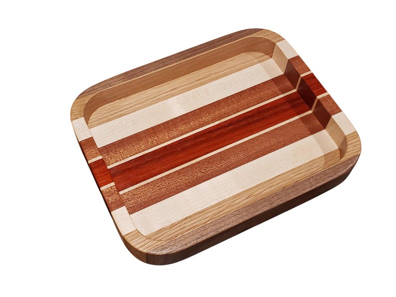 Op de afbeelding: Rechthoekige houten dienblad met afgeronde hoeken. De lade heeft afwisselende strepen van licht en donker hout, waaronder rode, bruine en natuurlijke tinten. De randen zijn van donkerder hout, waardoor een duidelijke rand ontstaat.