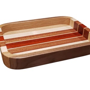 Op de afbeelding: Rechthoekige houten dienblad met een gestreept ontwerp. De lade heeft afwisselende banden van licht en donker hout, waaronder roodbruine en natuurlijke tinten. De randen zijn afgerond en de lade is gemaakt van verschillende houtsoorten.