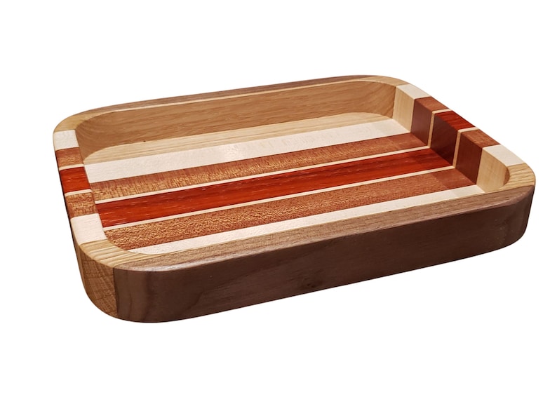 Op de afbeelding: Rechthoekige houten dienblad met een gestreept ontwerp. De lade heeft afwisselende banden van licht en donker hout, waaronder roodbruine en natuurlijke tinten. De randen zijn afgerond en de lade is gemaakt van verschillende houtsoorten.