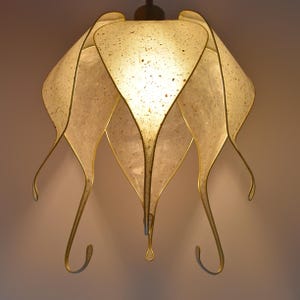 Könnte beinhalten: Ein weißer Lampenschirm aus Papier mit goldener Einfassung. Der Lampenschirm ist in Form einer Blume mit fünf Blütenblättern gestaltet. Die Blütenblätter sind gebogen und haben ein fließendes Design.