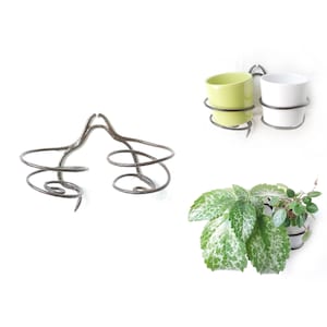 Könnte beinhalten: Zwei Metall-Pflanzenhalter mit Spiraldesign. Ein Halter ist leer, der andere hat einen grünen und einen weißen Keramiktopf.