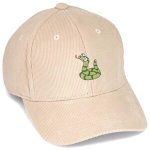 Peut inclure: Une casquette de baseball en velours côtelé beige ornée d'un serpent vert brodé avec de grands yeux blancs et une langue rouge. La casquette présente une calotte structurée avec des œillets cousus et une visière incurvée en tissu texturé.