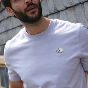 K&ouml;nnte beinhalten: Helllila T-Shirt mit einem kleinen, gestickten Schafmotiv auf der Brust. Das Schaf ist wei&szlig; mit schwarzen Details und einem &uuml;berraschten Gesichtsausdruck. Das T-Shirt hat kurze &Auml;rmel und einen Rundhalsausschnitt.