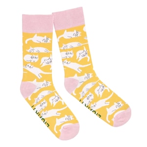 Peut inclure: Paire de chaussettes jaunes avec un motif répété d'illustrations de chats blancs. Les chaussettes ont des talons et des poignets roses. Le mot "LIVANTI" est imprimé sur le côté de chaque chaussette. Accessoire amusant et original.