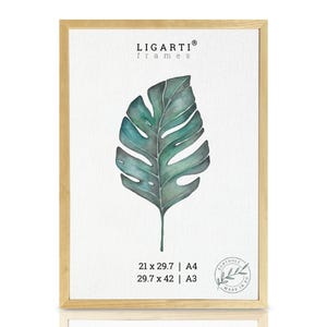 Könnte beinhalten: Ein gerahmter Aquarelldruck eines Monstera-Blattes in Grün- und Türkistönen. Der Rahmen ist aus hellem Holz. Die Druckmaße sind 21 x 29,7 cm (A4) und 29,7 x 42 cm (A3). Der Markenname "LIGARTI frames" steht oben.