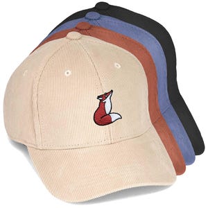 Könnte beinhalten: Ein Stapel aus vier Baseballkappen aus Kord in Beige, Rostrot, Blau und Schwarz. Jede Kappe ist auf der Vorderseite mit einer kleinen Stickerei eines rot-weißen Fuchses versehen und verfügt über eine strukturierte Krone und einen gebogenen Schirm.
