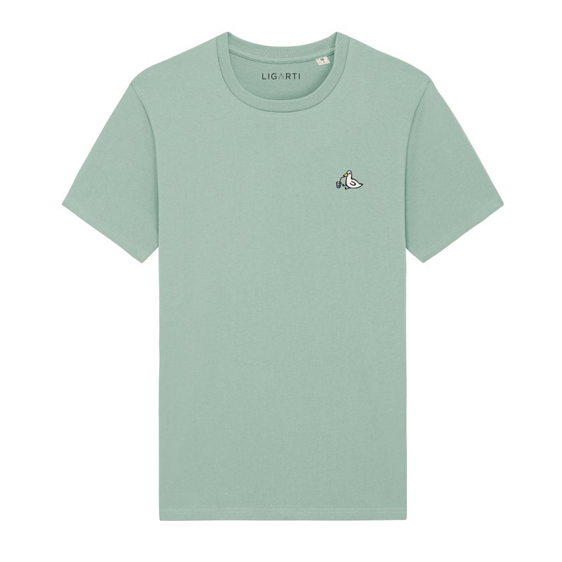 May include: A light green t-shirt with a small embroidered design of two birds on the left chest. The text "LIGARTI" is visible on the shirt.