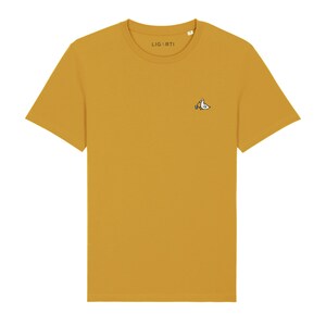 May include: A mustard yellow t-shirt with a small embroidered design of a bird holding a paintbrush on the left chest. The t-shirt has a crew neck and short sleeves. The brand name "LIGARTI" is printed on the tag.