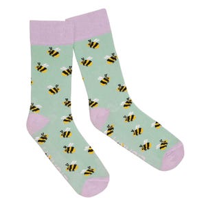May include: A pair of socks featuring a light green background adorned with a pattern of yellow and black bees. The heel and toe are light purple, with a matching light purple band at the top. The socks are made of a soft material.