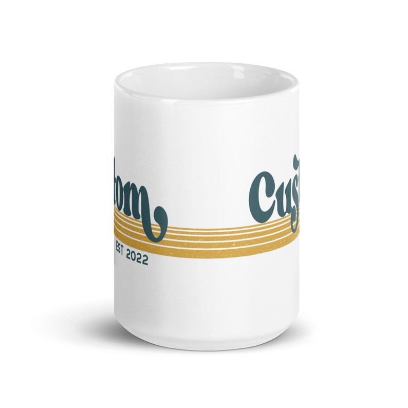 May include: White ceramic mug with a gold and teal design. The text "Custom" and "Est 2022" is printed on the mug.