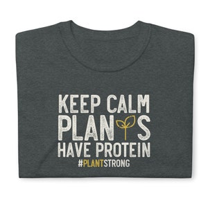 May include: Dark heather grey t-shirt with white text that reads "Keep Calm Plants Have Protein" and a small green plant graphic. The text "#PlantStrong" is below the main text.