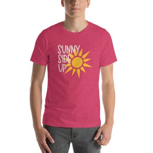May include: A pink heather t-shirt with a yellow sun graphic and the text "SUNNY SIDE UP" in white.