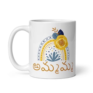 May include: White ceramic mug featuring a rainbow design in yellow, blue, and white. The rainbow has a flower with a yellow centre and blue petals on top. The text "అమ్మ ఒక మేఘం" is printed in black at the bottom of the mug.