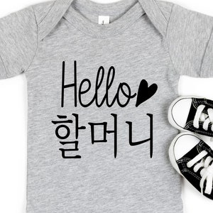 May include: A gray baby onesie with the text "Hello" and a black heart. Below the text is the Korean phrase "Hello" in black.