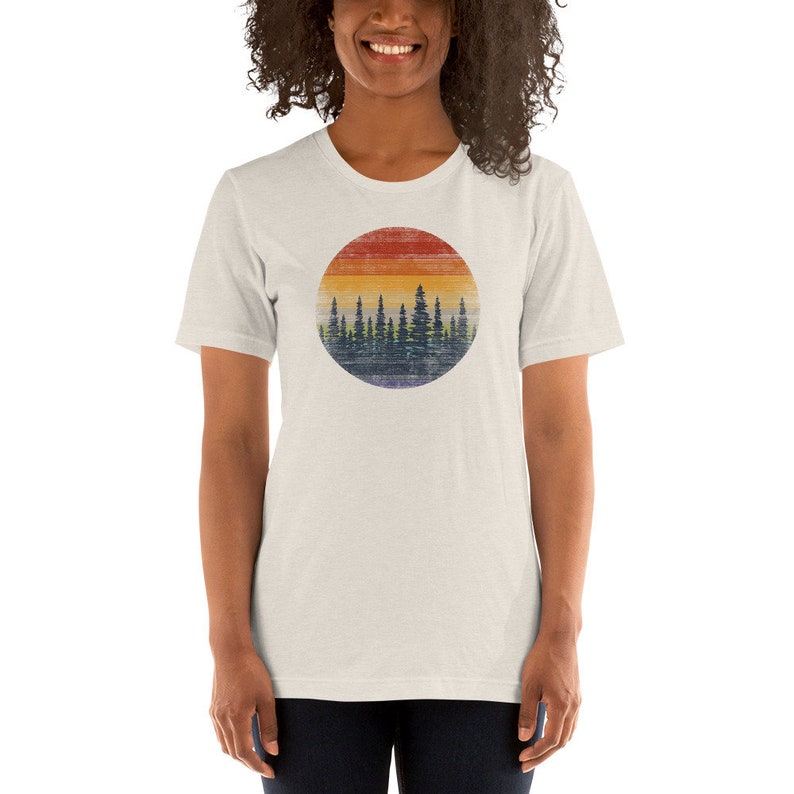 Puede incluir: Una camiseta blanca con un gr&aacute;fico de estilo vintage de una silueta de bosque contra una puesta de sol. El gr&aacute;fico est&aacute; en un c&iacute;rculo con un aspecto desgastado y texturizado.