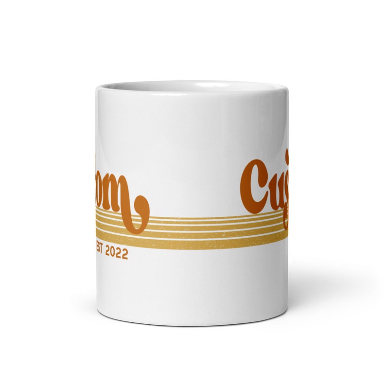 May include: White ceramic coffee mug with a brown and orange retro-style design. The mug has the text "Custom" and "Est 2022" on it.