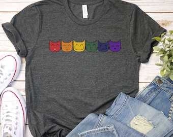 Könnte beinhalten: Ein dunkelgraues T-Shirt mit einem Regenbogen aus sechs Comic-Katzen mit verschiedenen Gesichtsausdrücken.