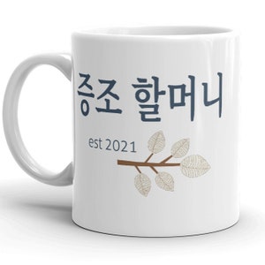 May include: White ceramic mug with a blue inscription that reads "쫑쫑 할머니 est 2021" and a brown twig with five beige leaves.