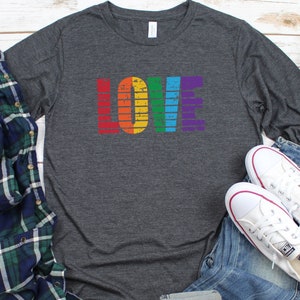 May include: A heather grey long-sleeve t-shirt with the word "LOVE" printed in rainbow colors. The letters are stylized with a vintage, distressed look.
