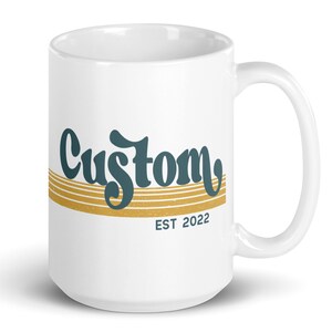 May include: White ceramic mug with a teal blue and gold design. The mug features the word "Custom" in a retro font with gold stripes and the text "EST 2022" below.