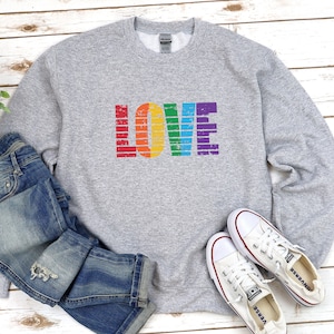 May include: A gray sweatshirt with the word "LOVE" printed on the front in rainbow colors. The letters are in a distressed, vintage style.