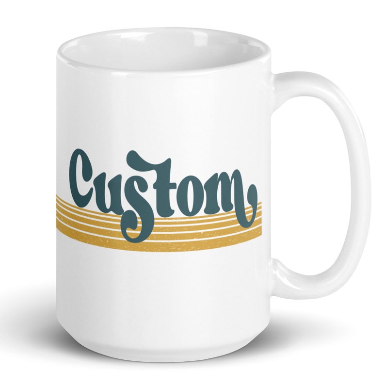 May include: White ceramic coffee mug with a gold and blue design. The word "Custom" is written in a retro font.