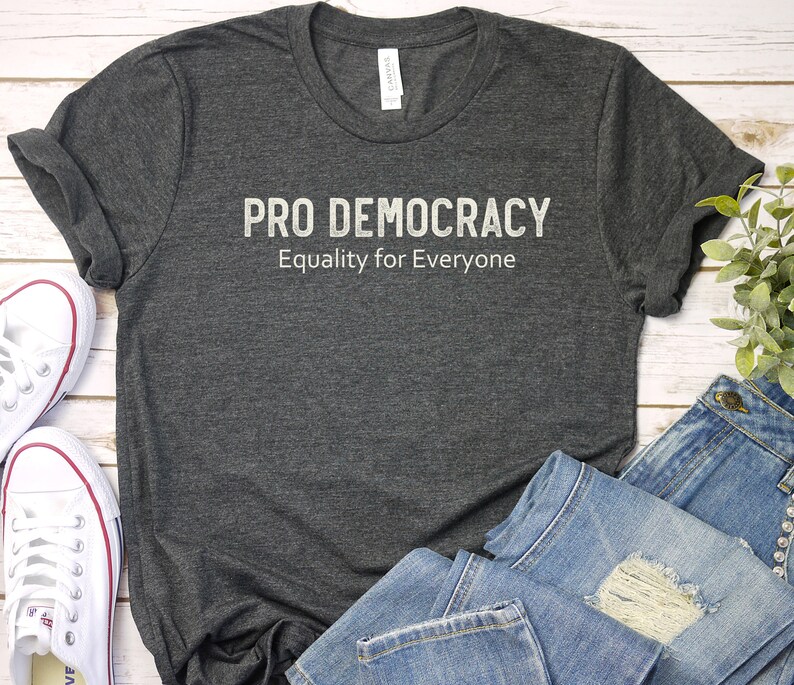 May include: A dark gray t-shirt with the text "PRO DEMOCRACY Equality for Everyone" printed in white.