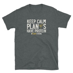 May include: A dark heather grey t-shirt with a white graphic that says "Keep Calm Plants Have Protein #PlantStrong".