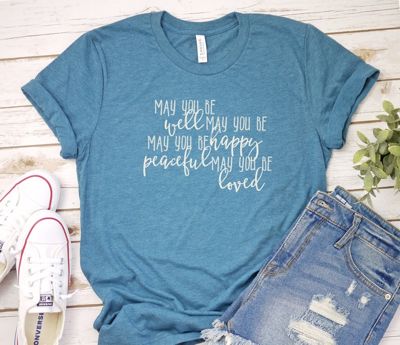 May include: A teal blue t-shirt with the text "MAY YOU BE well MAY YOU BE MAY YOU BE happy peaceful MAY YOU BE loved" printed in white on the front.