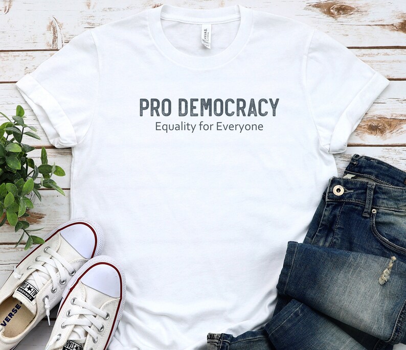 May include: White t-shirt with the text "PRO DEMOCRACY" and "Equality for Everyone" in gray lettering.