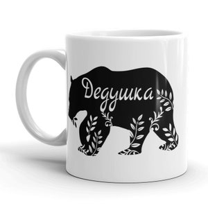 May include: White ceramic mug with a black silhouette of a bear with the word "Дедушка" in Russian on the bear's body.