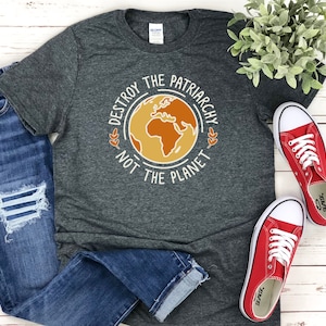 May include: A dark gray t-shirt with the text "Destroy the Patriarchy Not the Planet" printed on it. The text is surrounded by a circle with a stylized image of the Earth inside.
