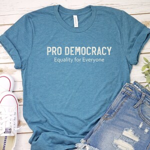 May include: A teal blue t-shirt with the text "PRO DEMOCRACY Equality for Everyone" printed in white on the front.