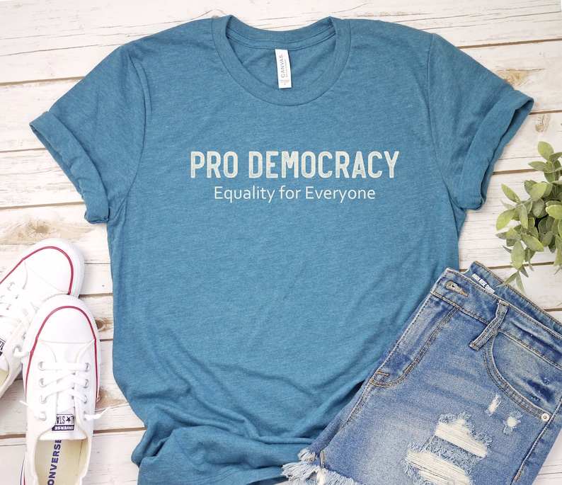 May include: A teal blue t-shirt with the text "PRO DEMOCRACY Equality for Everyone" printed in white on the front.