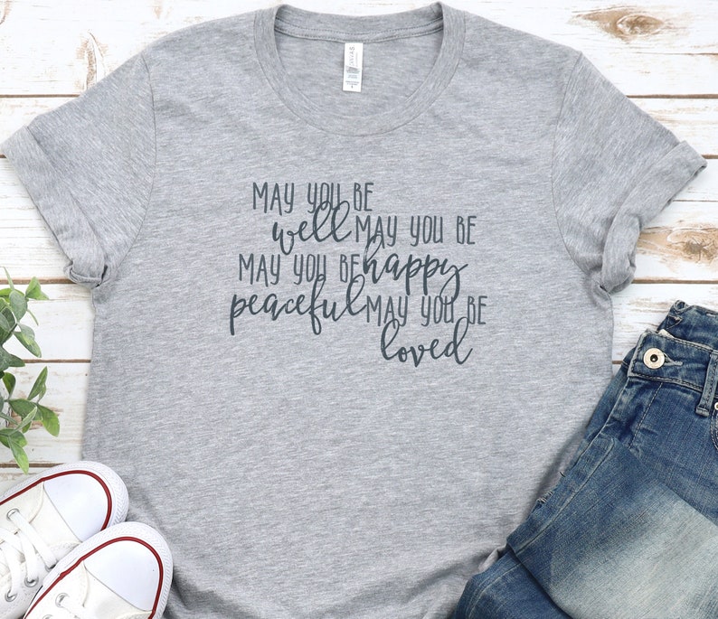 May include: Grey t-shirt with the text "MAY YOU BE well MAY YOU BE MAY YOU BE happy peaceful MAY YOU BE loved" printed on it.