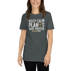 May include: A dark heather grey t-shirt with a white graphic that says "Keep Calm Plants Have Protein #PlantStrong".