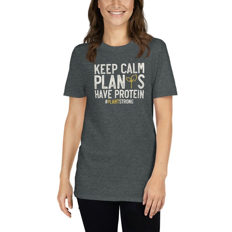 May include: A dark heather grey t-shirt with a white graphic that says "Keep Calm Plants Have Protein #PlantStrong".