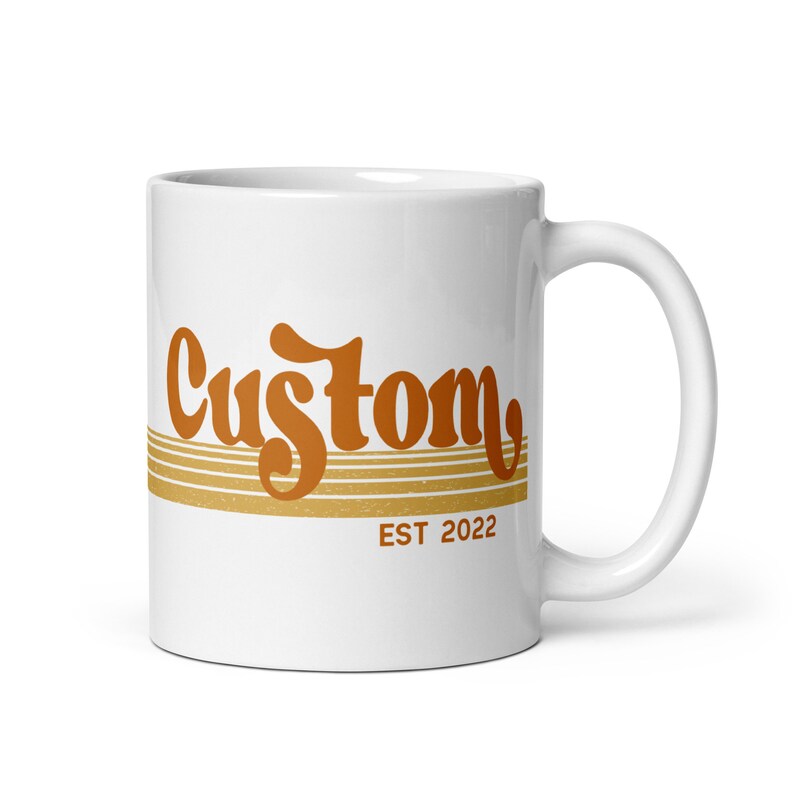 May include: White ceramic mug with a brown and orange retro-style graphic that says "Custom EST 2022".